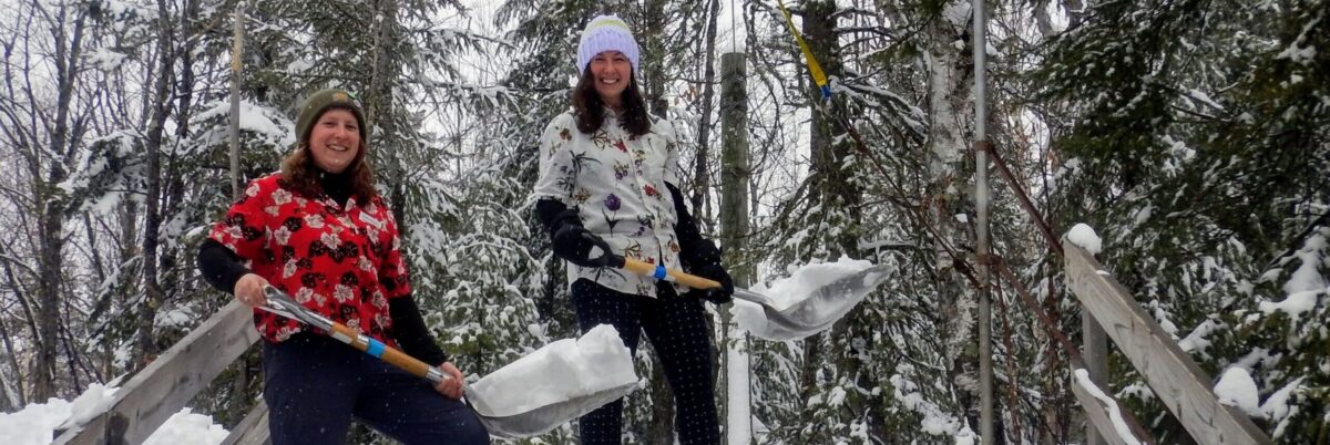 Two People Holding Snow Shovels with Snow at Wolf Ridge Winter