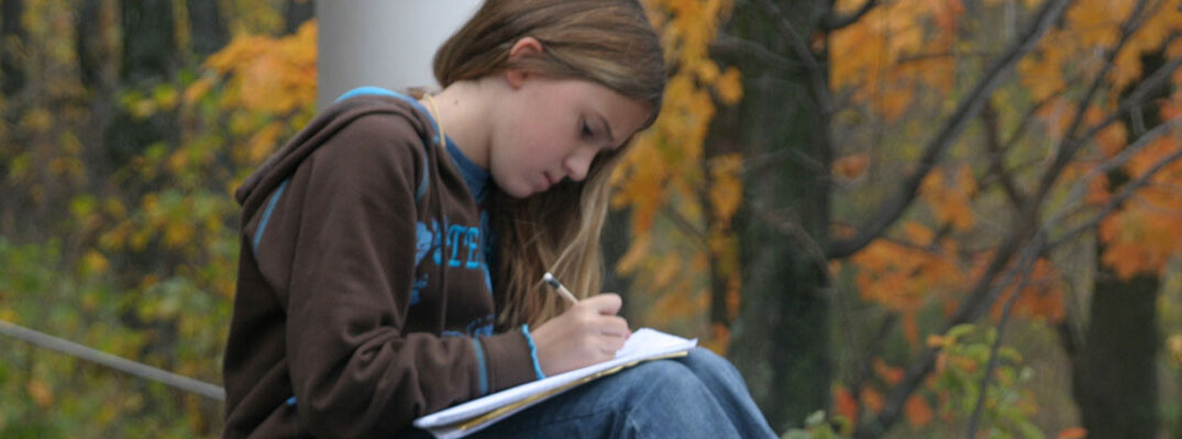Young woman journaling in autumn outside at Wolf Ridge
